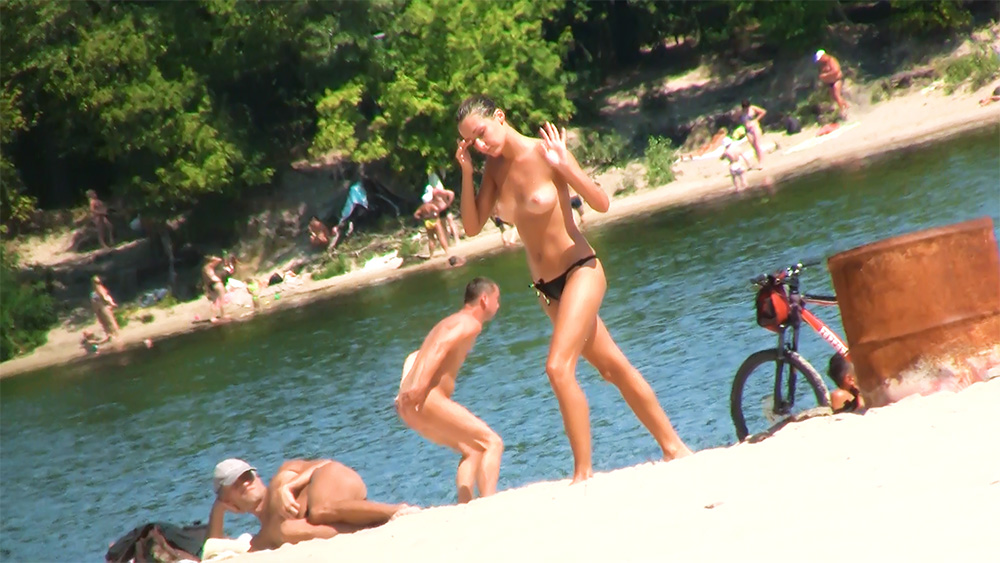 Staand op een topless strand aan het meer naast een fiets