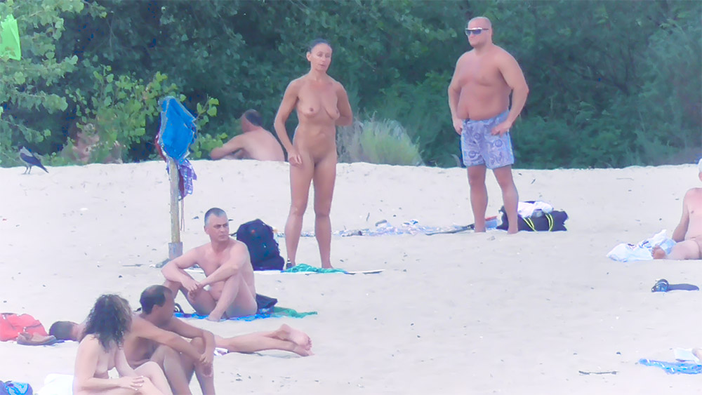 Standing Nude on the Sand Among Nude Beach Visitors