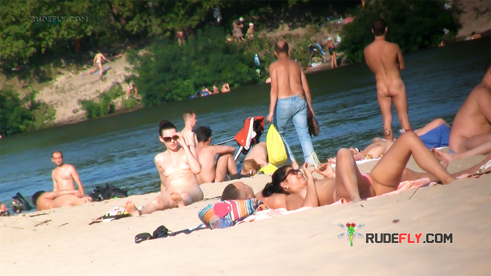 Sonnenbadende am FKK-Strand unter Freunden am sandigen Flussufer
