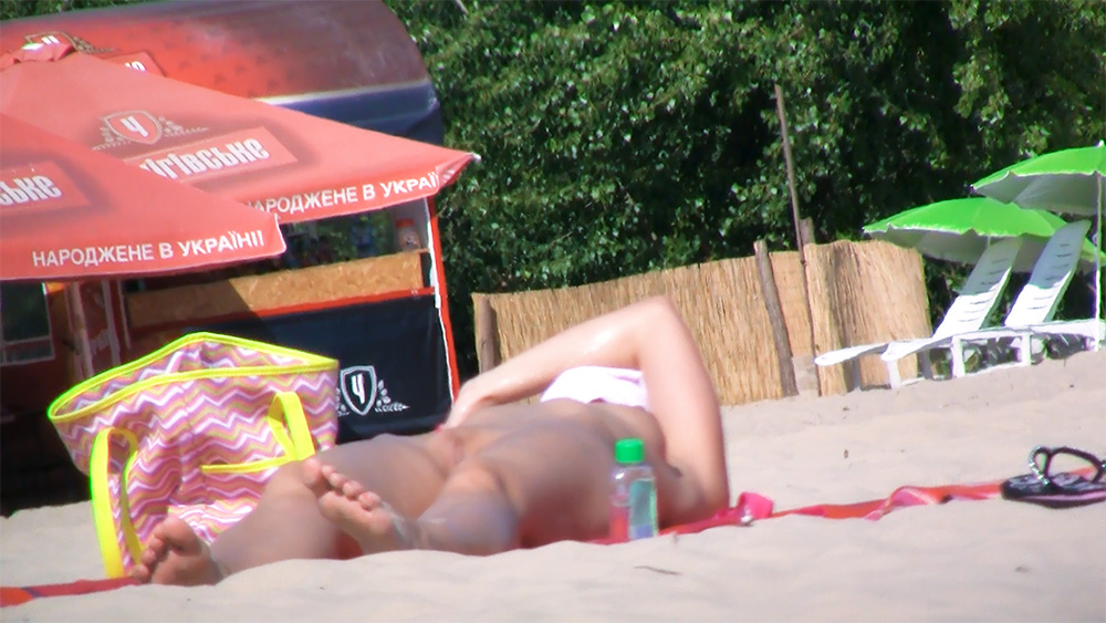 Opalování na nudistické pláži u červeného slunečníku