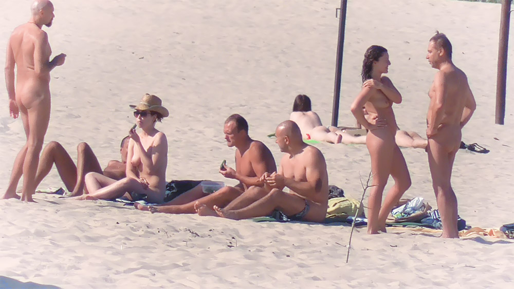 Para na plaży dla nudystów rozmawia, gdy inni odpoczywają na ręcznikach