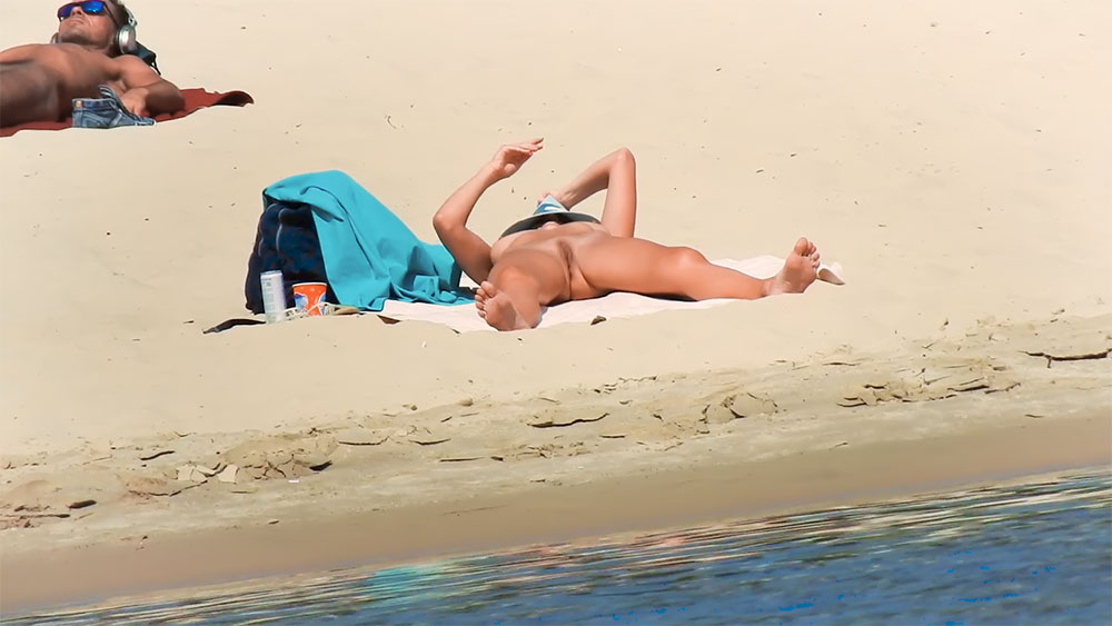 Břeh nudistické pláže s tyrkysovým ručníkem na písku
