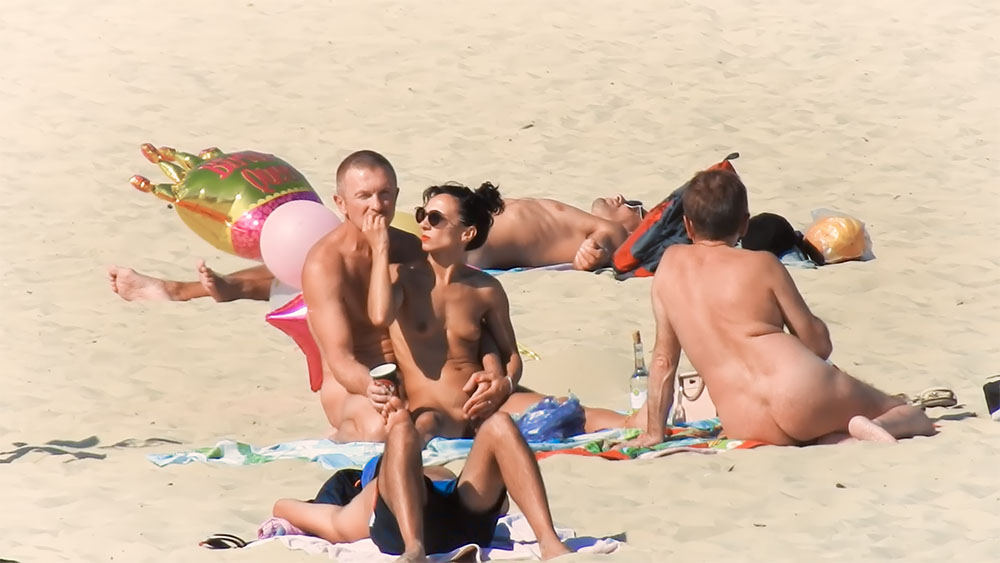 Five Nudists Lounging Near Inflatable Beach Toys